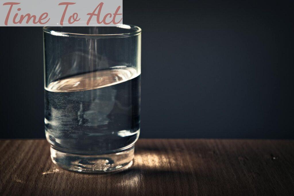 A clear glass of water sitting on a wooden table against a dark background.